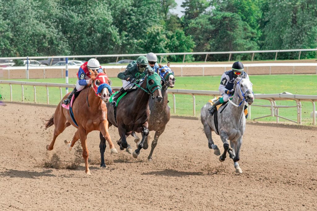 Jockeys and horses racing with intensity on a dirt track, showcasing speed and skill in an outdoor setting.