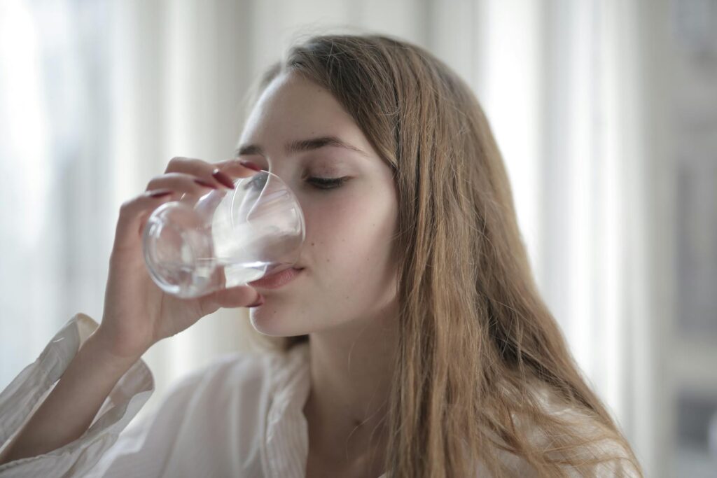 A woman enjoying a refreshing glass of water indoors during the day.
